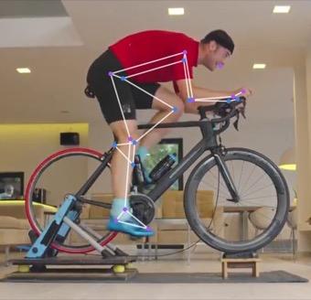 A rider on an indoor trainer at the bottom of the pedal stroke, filmed side-on, with the tracked skeleton drawn over the leg.